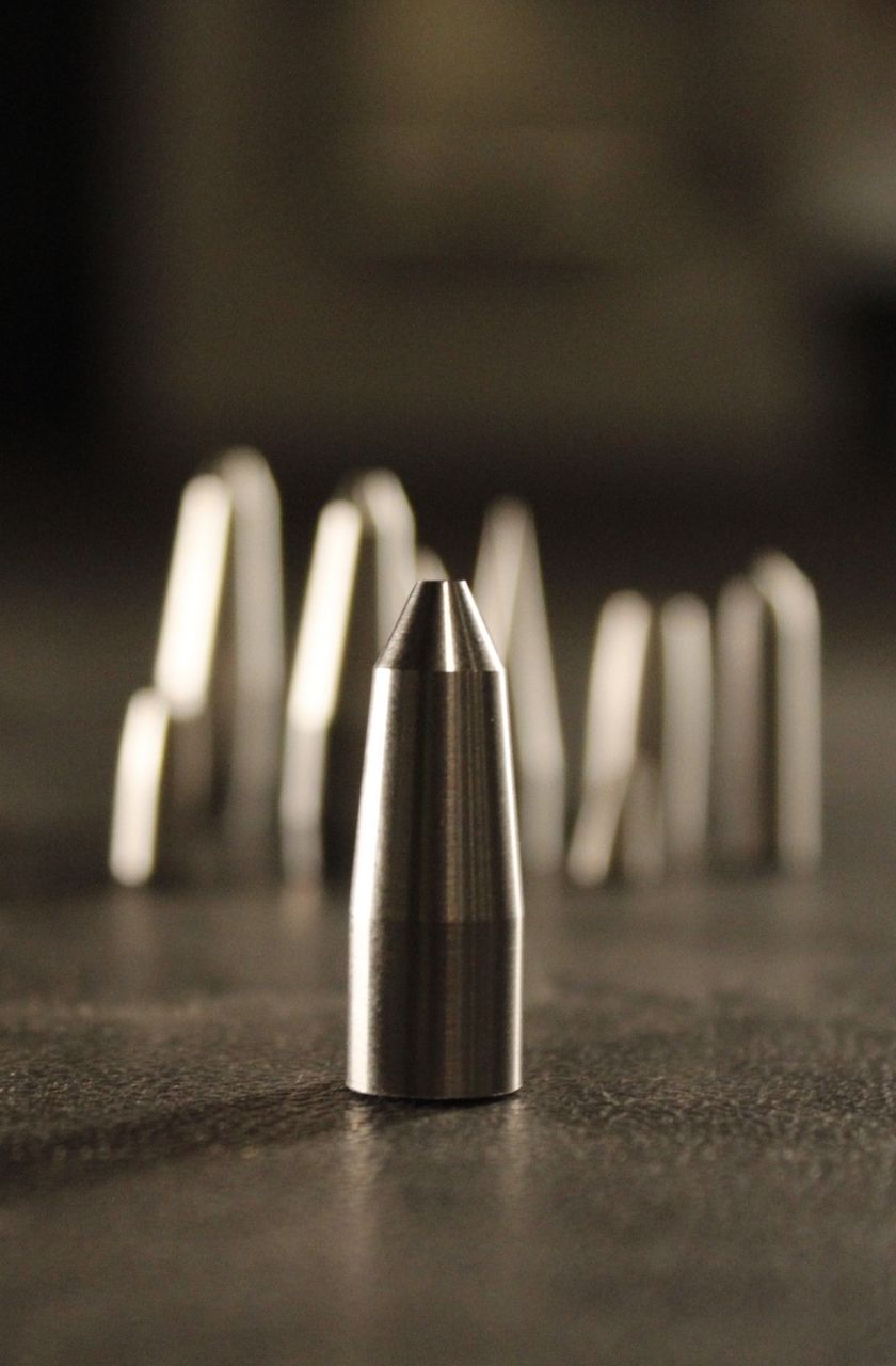 Precision-machined tungsten penetrator core with ogive nose profile, additional cores in soft focus, Tungsten Parts Wyoming