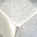 Machined tungsten cube held in caliper jaws for dimensional measurement
