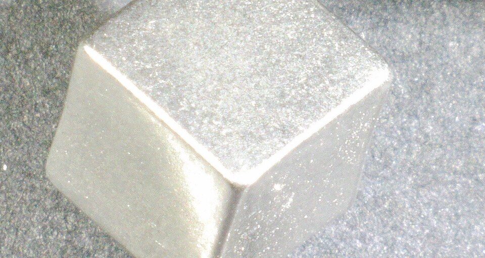 Machined tungsten cube held in caliper jaws for dimensional measurement