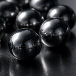Polished precision tungsten carbide balls clustered on a dark machinist surface plate