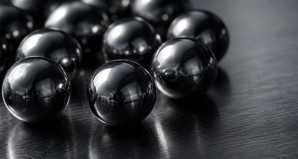 Polished precision tungsten carbide balls clustered on a dark machinist surface plate