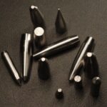 Machined tungsten cores in assorted profiles on a black leather surface