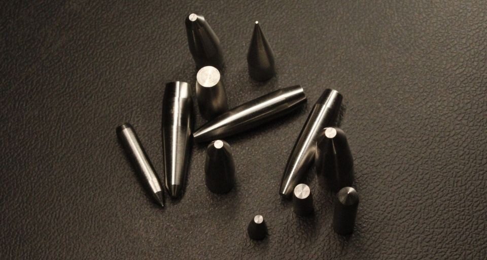 Machined tungsten cores in assorted profiles on a black leather surface